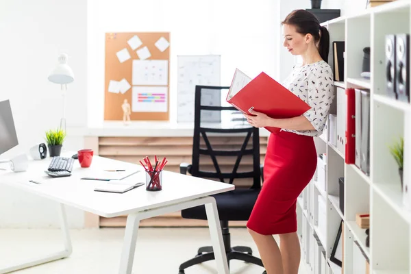 A young girl standing in the office and holding a red folder with documents. — Stock Photo, Image