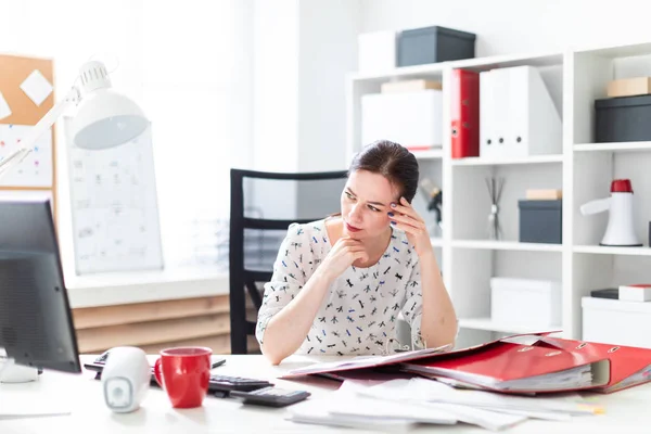 Молодая девушка сидит в офисе за компьютерным столом, работает с документами и держит его за голову . — стоковое фото