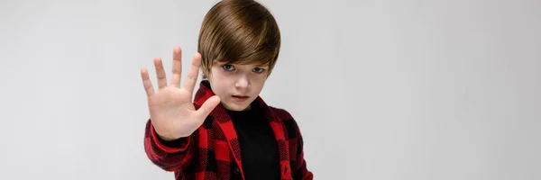 Милий впевнений сумний маленький кавказький хлопчик у картатій сорочці, що показує знак зупинки на сірому фоні — стокове фото