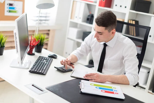 Un joven sentado en una computadora Escritorio en la oficina y trabajando con documentos . — Foto de Stock