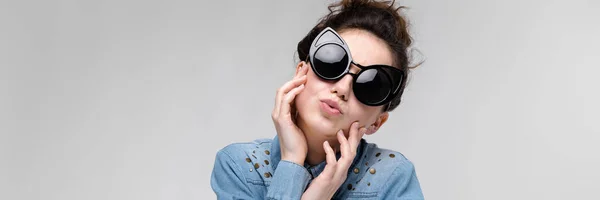 Chica morena joven en gafas negras. Gafas de gato. El pelo está recogido en un moño. La chica sostiene su cara . —  Fotos de Stock