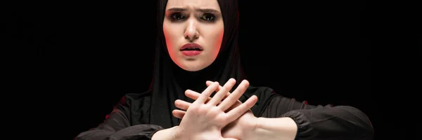 Porträt der schönen verzweifelten verängstigten jungen Muslimin, die schwarzen Hijab trägt und Stoppschild auf schwarzem Hintergrund zeigt — Stockfoto