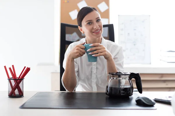 Una joven sentada en una mesa en la oficina y sosteniendo una taza . — Foto de Stock