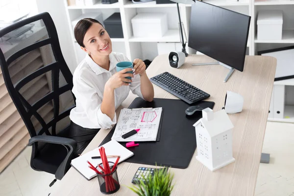 Una joven sentada en la oficina en la computadora y sosteniendo una taza . — Foto de Stock