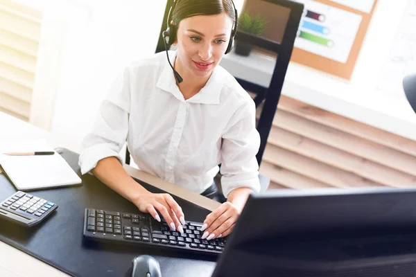 A young girl in headphones with a microphone sitting at a computer table. — Stock Photo, Image