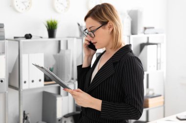 Bir genç kız ofiste ayakta ve telefonda konuşurken.