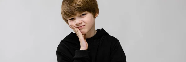 Adolescente encantador com cabelo loiro e olhos escuros. O adolescente apoiou a bochecha com os dedos. O adolescente está descontente — Fotografia de Stock