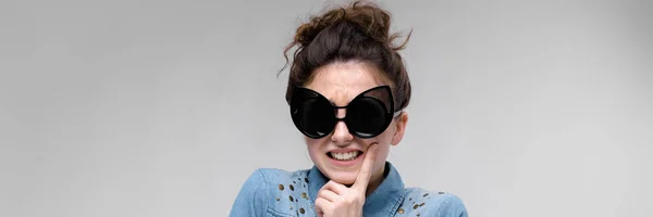 Junges brünettes Mädchen mit schwarzer Brille. Katzenbrille. Die Haare sind zu einem Dutt zusammengebunden. das Mädchen hält sich die Hand an den Bauch. — Stockfoto