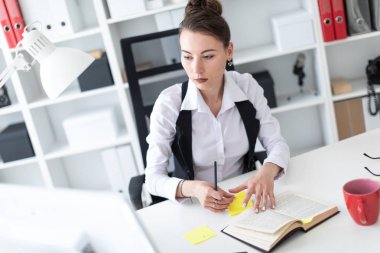 Genç bir kız ofiste bir masada oturuyor, bir kalem tutan ve çıkartmaları ile çalışma.