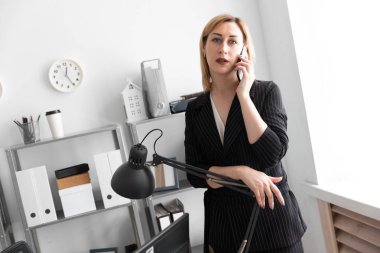 Genç bir kız ofiste telefonda konuşurken ve yüksek lambayı elini koydu.