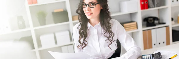 Молодая девушка работает за компьютером в офисе и держит в руке ручку и блокнот. . — стоковое фото