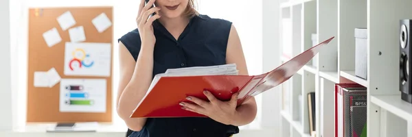 En ung flicka på kontoret pratar i telefonen och hålla en mapp med dokument. — Stockfoto