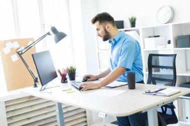 Ofiste ayakta ve bilgisayar masasında çalışan genç bir adam.
