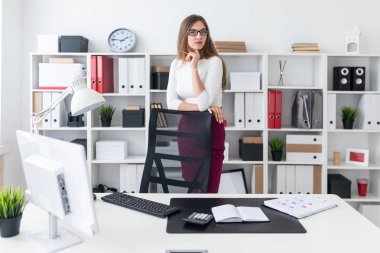 Genç bir kız tablonun duruyor ve elleri yüksek sandalyenin üstüne koy. Kız gözlük ve bir kalem vardır.