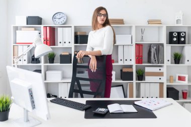 Genç bir kız tablonun duruyor ve elleri yüksek sandalyenin üstüne koy. Kız gözlük ve bir kalem vardır.