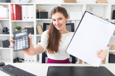 Bir masada oturan ve bir hesap makinesi ve boş bir sayfa tutan genç bir kız.