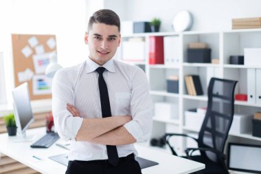 Genç adam ofiste masanın üzerine eğilerek standları ve elleri göğsünde katlanmış.