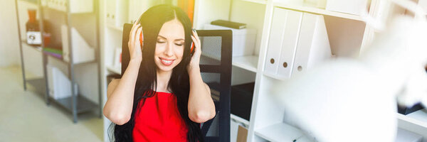 Красивая молодая девушка в наушниках сидит в офисе за столом
.