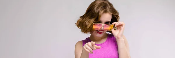Encantadora joven en vestido rosa sobre fondo gris. Chica alegre en gafas cuadradas . —  Fotos de Stock