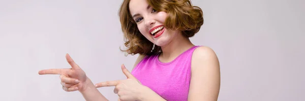 Charming young girl in pink dress on gray background. A young girl shows her fingers aside — Stock Photo, Image