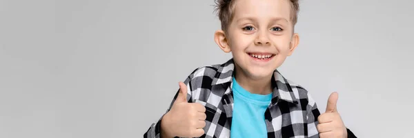Ein gutaussehender Junge in kariertem Hemd, blauem Hemd und Jeans steht vor grauem Hintergrund. der Junge lächelt und zeigt Klasse — Stockfoto