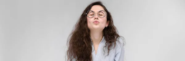 Menina morena nova com óculos. A menina puxa os lábios para um beijo. A menina fechou os olhos . — Fotografia de Stock