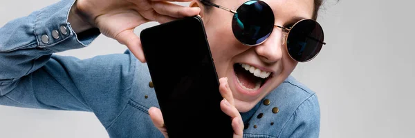 Young brunette girl in round glasses. Hairs are gathered in a bun. Girl with a black phone. — Stock Photo, Image