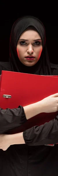 Siyah arka plan üzerinde tutmak gizli kavram olarak siyah Tesettür holding klasörleri giyen korkmuş genç Müslüman kadın portresi güzel umutsuz korkuttu — Stok fotoğraf