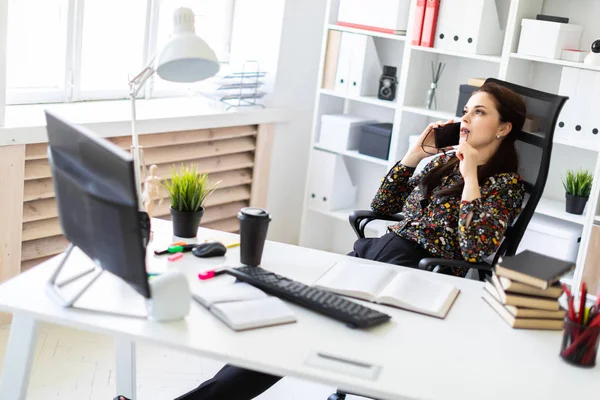 Een jong meisje zittend op kantoor op de computer Desk en praten over de telefoon. — Stockfoto