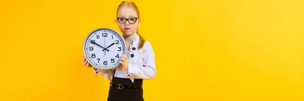 Girl with red hair on a yellow background. A charming girl in transparent glasses is holding a watch. — Stock Photo, Image