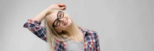 Mooie tiener meisje met lang haar en dragen bril. Een tienermeisje in een plaid shirt en een grijs T-shirt. Een tiener meisje stak haar hand achter haar hoofd. — Stockfoto