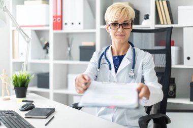 Beyaz bir elbise içinde genç bir kız masada oturur ve ileri bir kalem ve bir belge uzanır.