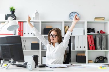 Bir genç kız bir bilgisayarda ofis masasında oturan ve ellerini kaldırdı.