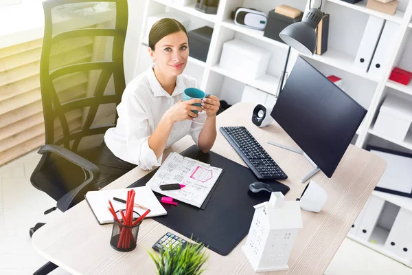 Een jong meisje zittend op kantoor op de computer en holding een kop. — Stockfoto