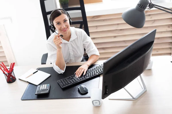 Una joven en auriculares con un micrófono sentado en una mesa de ordenador . — Foto de Stock