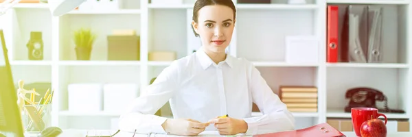 Una giovane ragazza in ufficio si siede a un tavolo e tiene in mano una penna . — Foto Stock