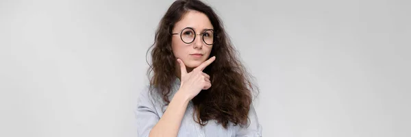 Retrato de una joven con gafas. Hermosa joven sobre un fondo gris. Una joven con una blusa clara y pantalones oscuros . — Foto de Stock