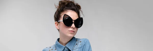 Junges brünettes Mädchen mit schwarzer Brille. Katzenbrille. Die Haare sind zu einem Dutt zusammengebunden. verschränkte das Mädchen die Arme. das Mädchen lacht. — Stockfoto