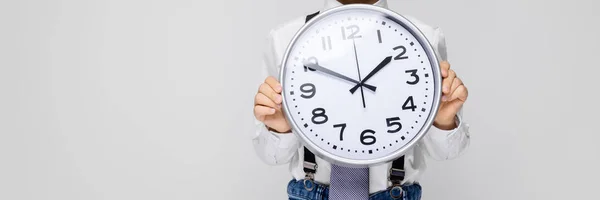 Ein charmanter Junge in weißem Hemd, Hosenträgern, Krawatte und heller Jeans steht vor grauem Hintergrund. der Junge hält eine Armbanduhr — Stockfoto