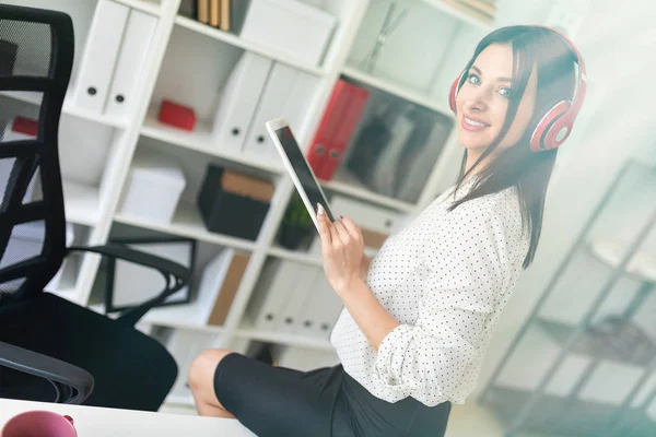 Une jeune fille avec écouteurs assis sur la table et tenant une tablette . — Photo