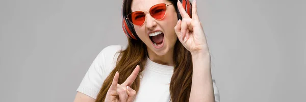 Retrato de emocionalmente hermosa feliz modelo de tamaño grande en auriculares y gafas de sol de pie en el estudio mirando en la cámara escuchando música —  Fotos de Stock