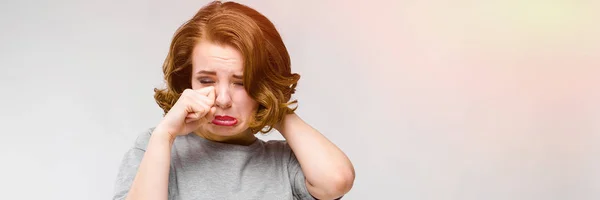 Encantadora joven con una camiseta gris sobre un fondo gris. La chica está llorando. — Foto de Stock