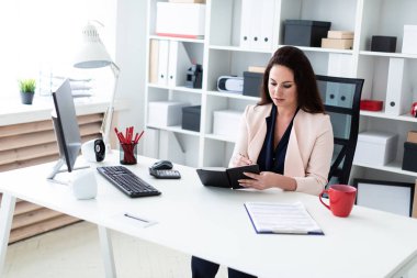Genç bir kız Danışma bilgisayar başında oturan, bir kalem tutan ve bir notebook, tablet ve belgeler ile çalışma.
