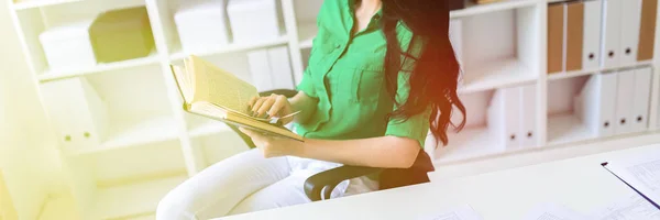 Молодая девушка сидит за рабочим столом и держит книгу . — стоковое фото