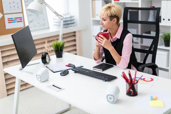 La chica trabaja en la oficina en la computadora y sostiene una taza . — Foto de Stock