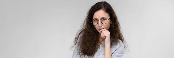 Junges brünettes Mädchen mit Brille. das Mädchen legte einen Finger auf ihre Wange. — Stockfoto