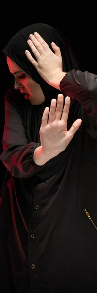 Retrato de una hermosa mujer musulmana asustada y desesperada con hiyab negro mostrando una señal de stop sobre un fondo negro — Foto de Stock