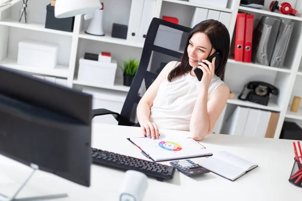 Una joven sentada en la oficina en el escritorio de la computadora, hablando por teléfono y trabajando con documentos . — Foto de Stock