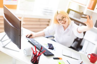 Ofiste oturan ve bir banka kartı tutan genç bir kız.