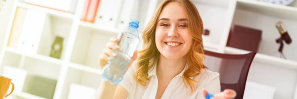 Una bella ragazza si siede in ufficio e tiene in mano una bottiglia d'acqua . — Foto Stock